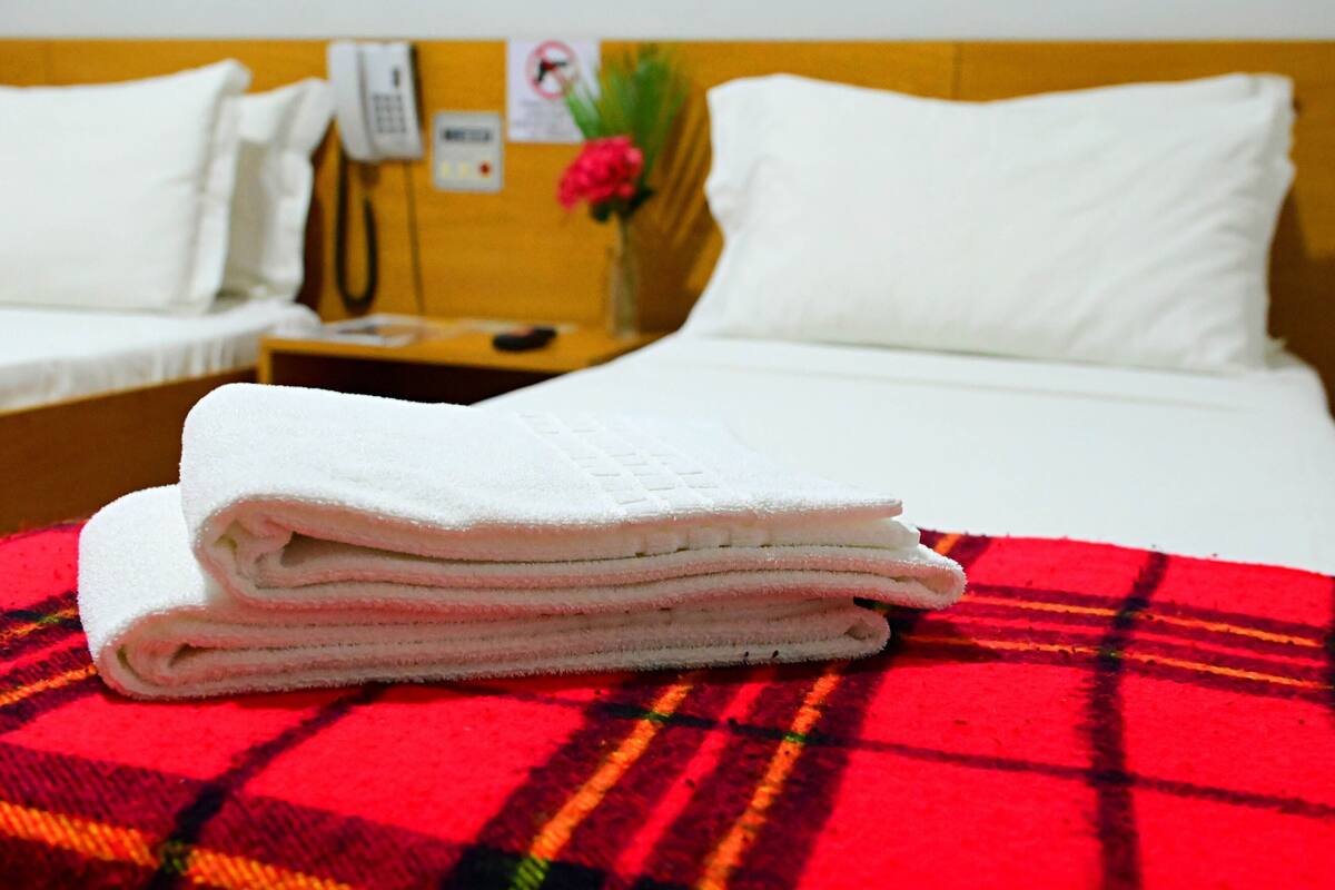 Habitación de hotel con dos camas, una colcha escocesa roja, toallas blancas, un teléfono y un florero.