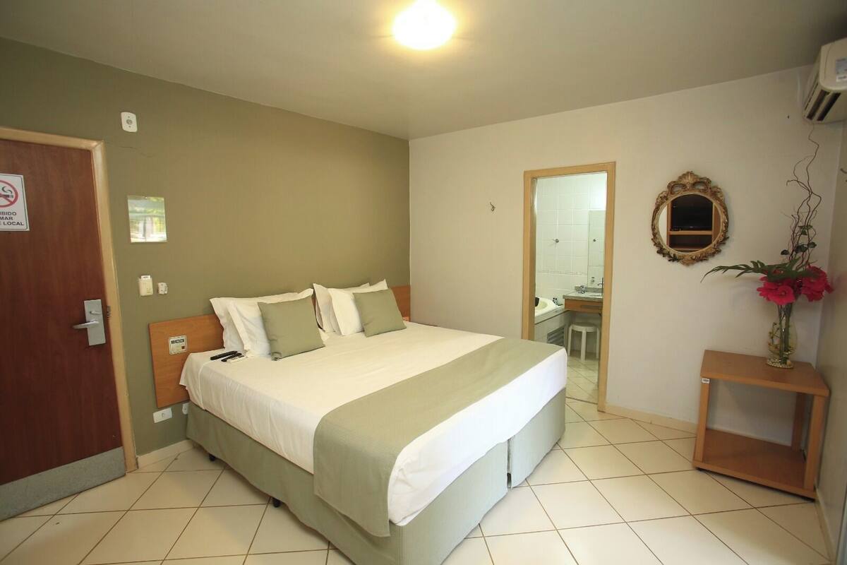 Una habitación de hotel con una cama, una mesita de noche, un espejo y un pequeño taburete.