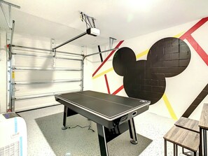 A room with a table, a projector mounted on the ceiling, and a wall with a large Mickey Mouse design.