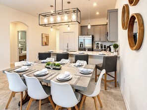 Una cocina moderna con electrodomésticos de acero inoxidable, un comedor con mesa de madera y sillas blancas, y una lámpara colgante.