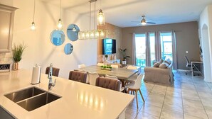 A modern kitchen with a large island, pendant lights, and a dining area with a sofa and chairs.