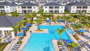 A large swimming pool surrounded by lounge chairs and umbrellas, with a view of residential buildings in the background.