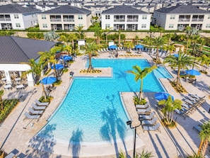 A large swimming pool surrounded by lounge chairs and umbrellas, with a view of residential buildings in the background.