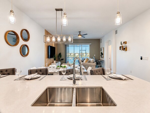 A modern kitchen with a central island, stainless steel sinks, and pendant lighting.