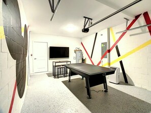 A billiards table in a room with a white wall, a television, and a door.