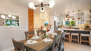 Una cocina moderna con comedor, que incluye una mesa de madera dispuesta para seis personas, una isla central con taburetes e iluminación colgante.