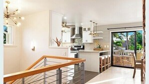 Una cocina moderna con una isla central, un comedor con mesa y sillas, y una escalera con barandilla.