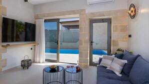 Una sala moderna con un sofá gris, un televisor de pantalla plana y vista a la piscina.