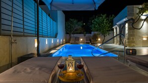 Un área de piscina exterior con una tumbona, una mesa con dos copas de vino y un farol.