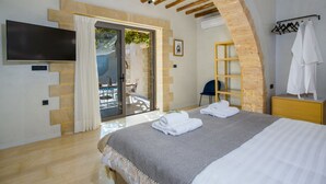 Un dormitorio con cama, televisor, techo de madera, pared de piedra, balcón y perchero.