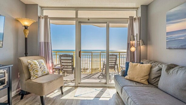 Une chambre avec balcon donnant sur la plage, meublée d’un canapé, d’un fauteuil et d’une table.