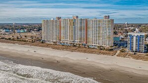 Un grand hôtel à plusieurs étages, situé près d’une plage où l’on peut voir les vagues.