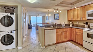 A kitchen with wooden cabinets, a microwave, and a dishwasher. There is a washing machine in the corner. - SandCastle 1804 - Beautiful updates, Breathtaking view, tons of amenities (Indian Shores)