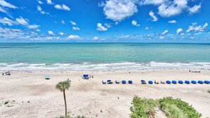A beach with a row of blue umbrellas and a palm tree. - SandCastle 1804 - Beautiful updates, Breathtaking view, tons of amenities (Indian Shores)