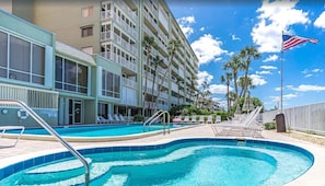 A hotel with a swimming pool, multiple balconies, and palm trees.