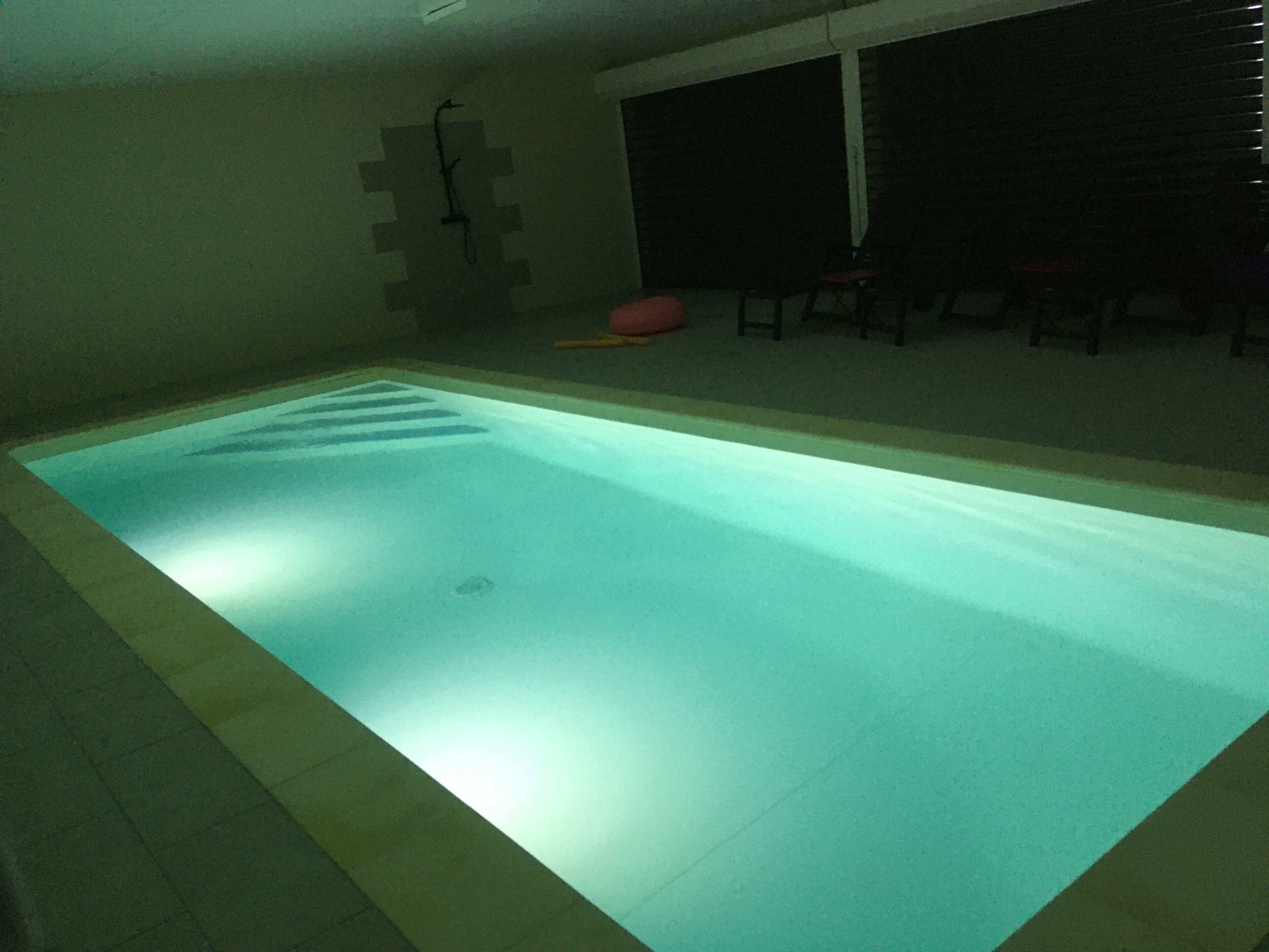 A rectangular indoor swimming pool with a tiled border, a drain in the center, and a tiled wall with a geometric pattern behind it.
