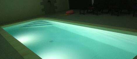 A rectangular indoor swimming pool with a tiled border, a drain in the center, and a tiled wall with a geometric pattern behind it.