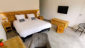 A bedroom with a large bed, bedside tables, a TV, a chair, and a small wooden table. - Domaine des Bois Argentés (Pruniers-en-Sologne)