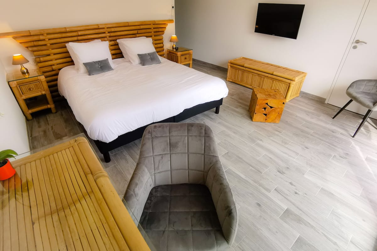 A bedroom with a large bed, bedside tables, a TV, a chair, and a small wooden table.