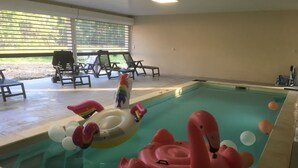 An indoor swimming pool with inflatable toys, lounge chairs, and a view of greenery outside. - Domaine des Bois Argentés (Pruniers-en-Sologne)
