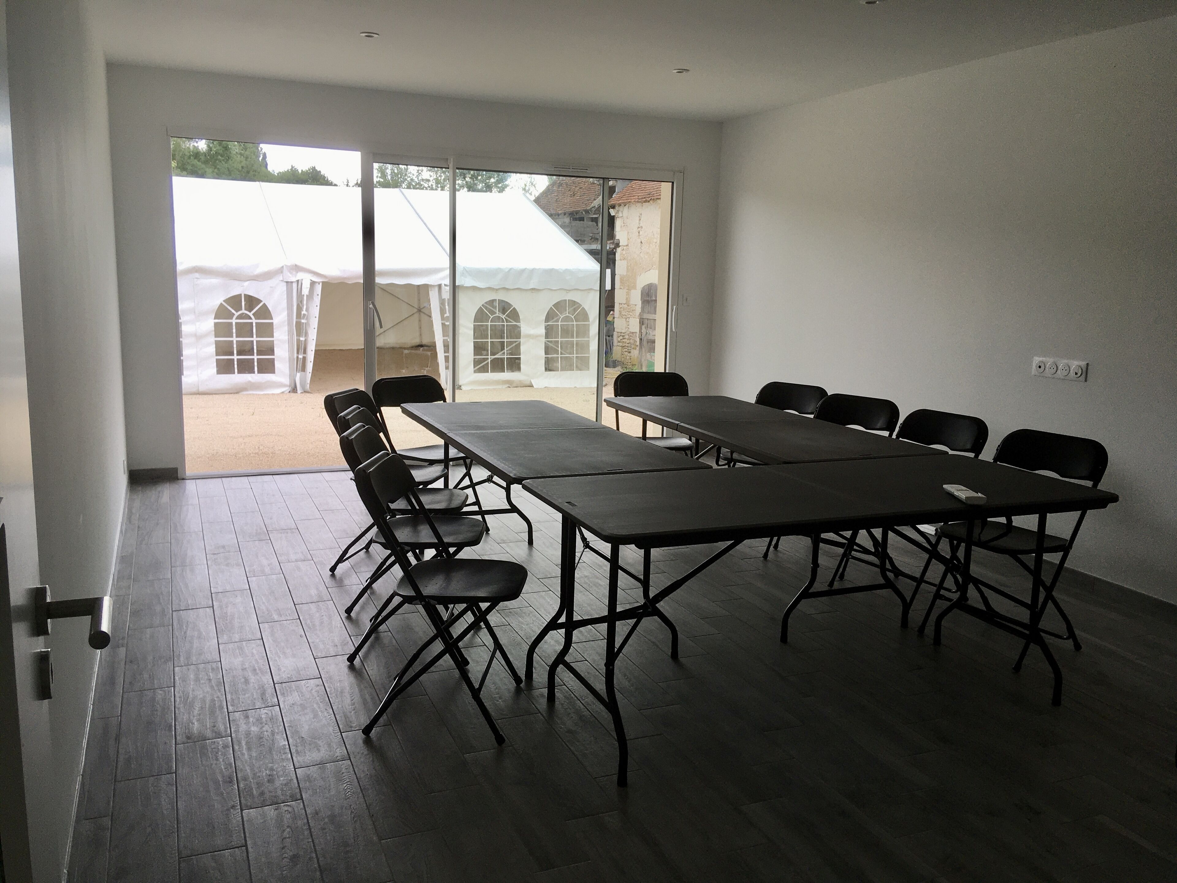 A conference room with a long table and chairs, large windows, and a view of tents outside.