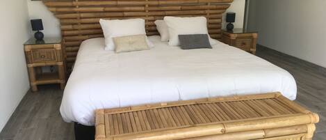 A neatly made bed with a wooden headboard, two bedside tables with lamps, and a woven bench at the foot of the bed.