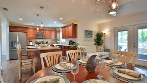 Una cocina moderna con armarios de madera, un comedor para seis personas con una isla central, y un ventanal que proporciona luz natural.