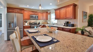 Una cocina moderna con encimeras de granito, electrodomésticos de acero inoxidable, armarios de madera e iluminación colgante.