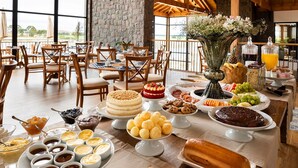 A spacious dining area with wooden beams, large windows, and a variety of food and drinks on a buffet table. - Cerro Azul Hotel Fazenda (Capao Alto)