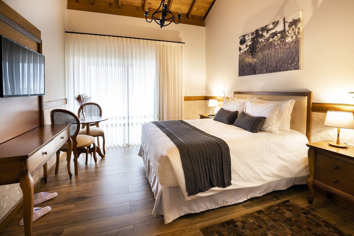 A hotel room with a large bed, bedside lamps, a desk with a chair, and a TV.