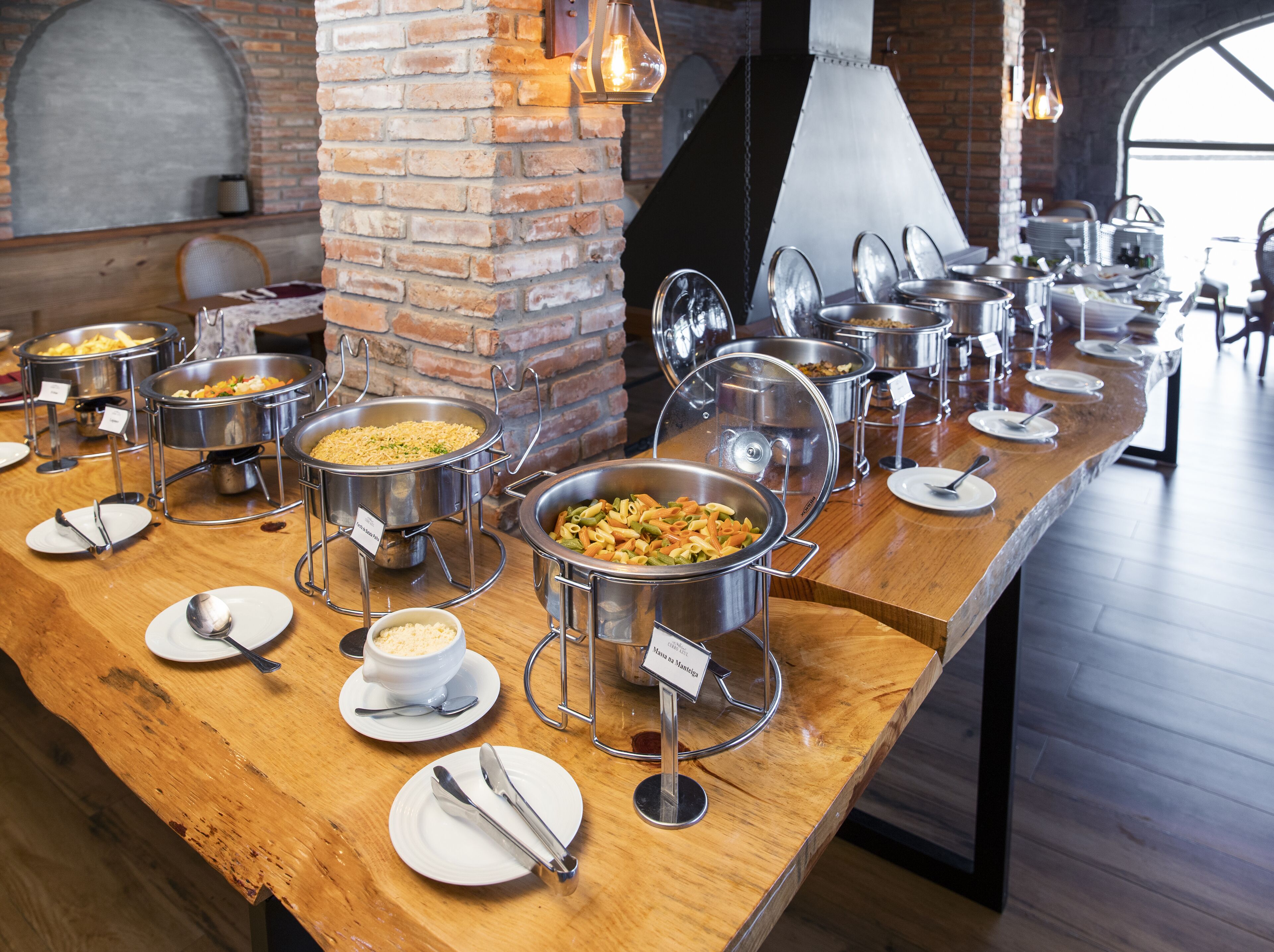 A buffet setup with various food stations, a brick wall, and a large window.