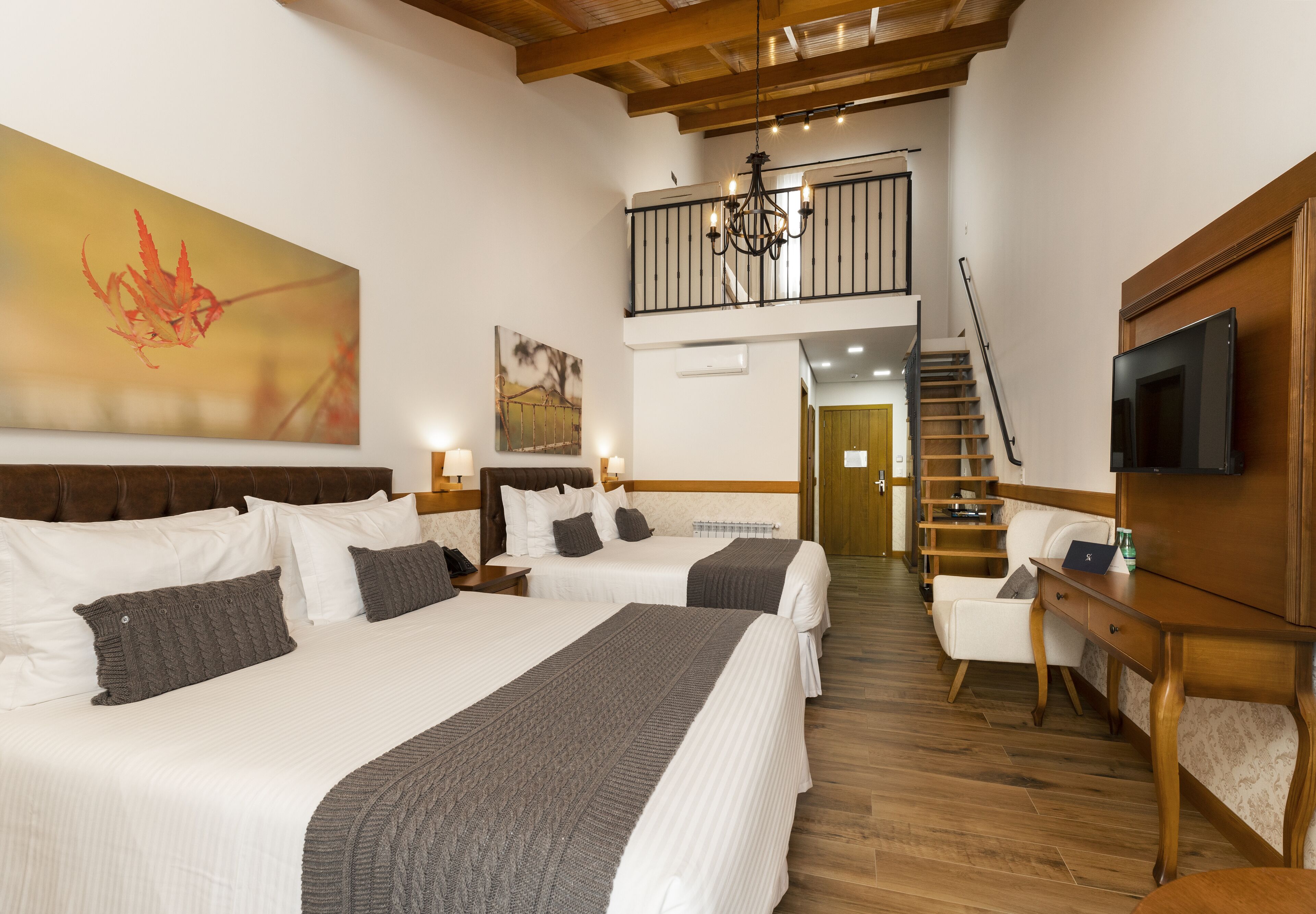 A hotel room with two beds, a TV, a desk, and a staircase leading to an upper level.