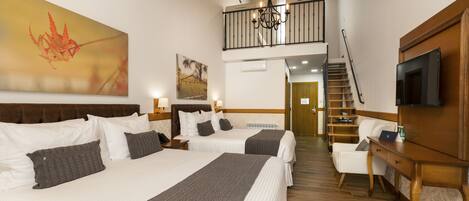 A hotel room with two beds, a TV, a desk, and a staircase leading to an upper level.