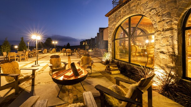 An outdoor patio with stone walls, wooden furniture, and a fire pit. - Cerro Azul Hotel Fazenda (Capao Alto)