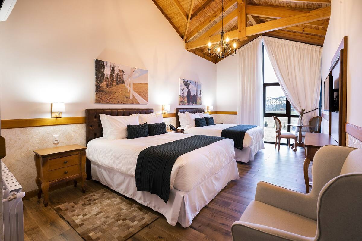 A bedroom with two beds, a wooden floor, a chandelier, and a view of the outdoors.