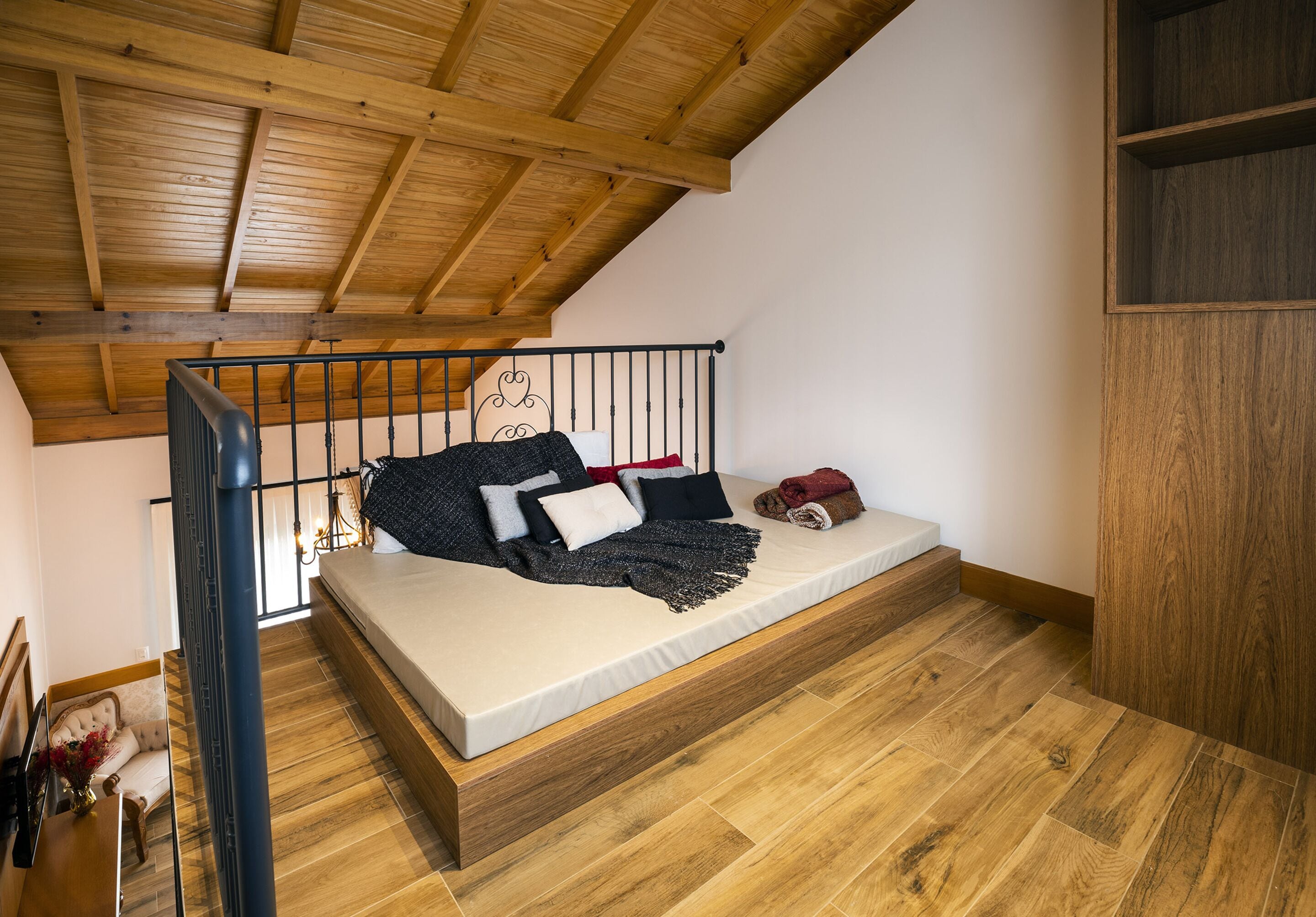 Une chambre à coucher aménagée dans un espace de type « loft », avec un plafond en bois, un lit doté d’un matelas et d’oreillers, un plancher en bois et un escalier.