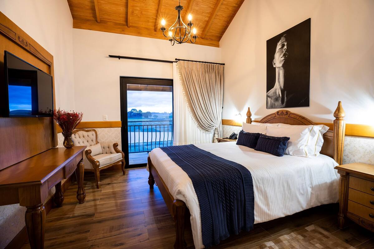 A bedroom with a large bed, wooden furniture, a TV, and a view through a window.