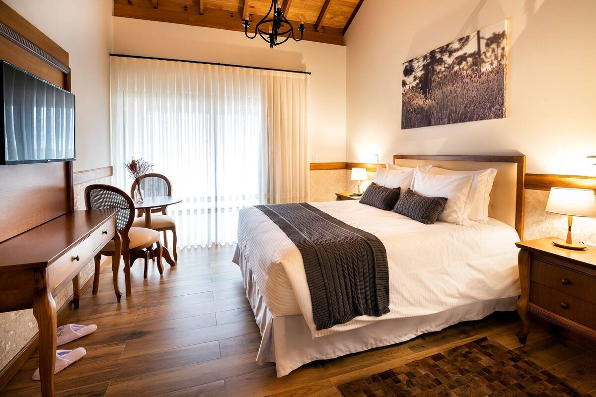 A hotel room with a large bed, bedside lamps, a wooden desk, a chair, and a TV.
