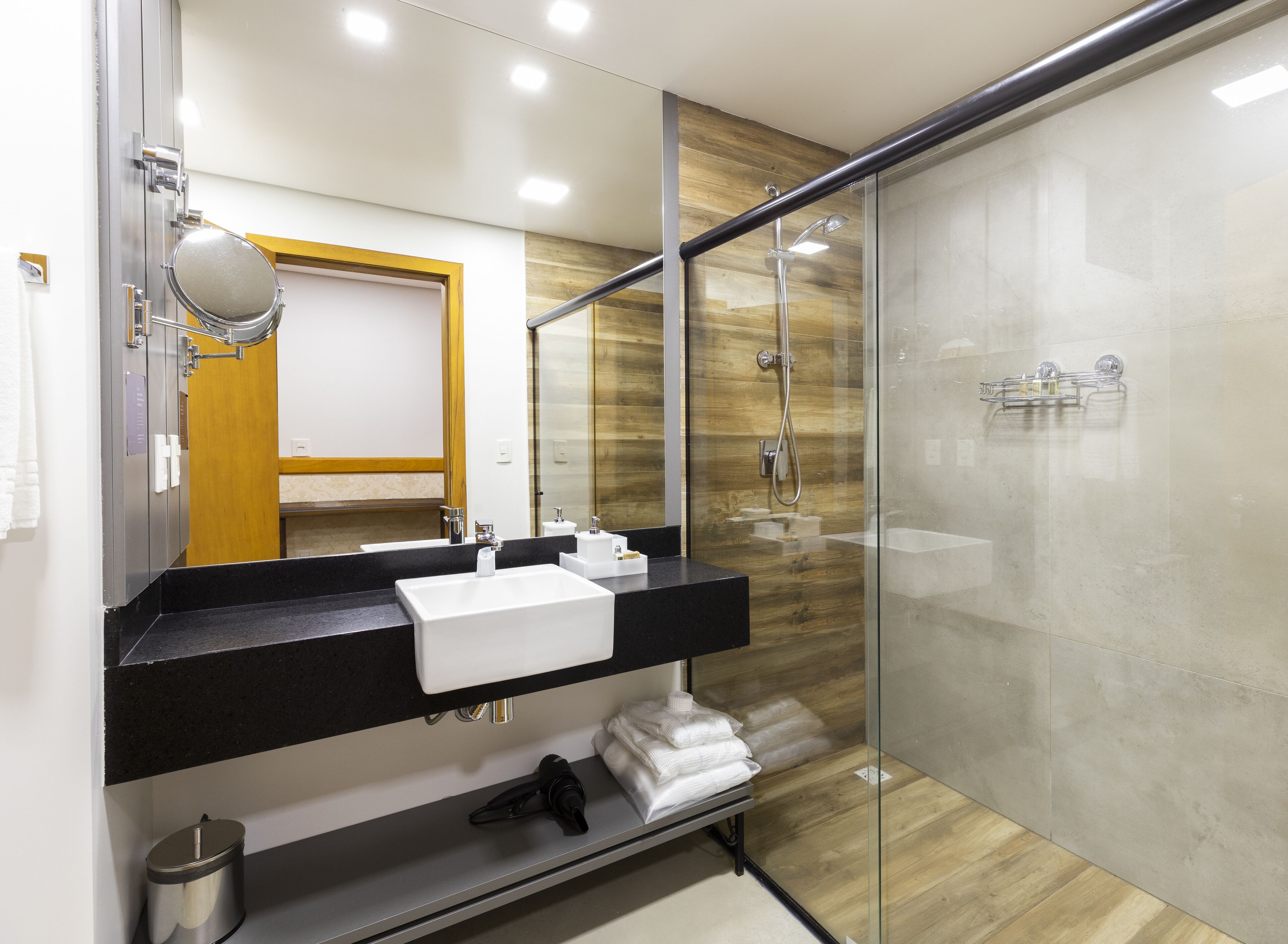 Un baño moderno con ducha de vidrio, encimera negra y lavabo blanco.