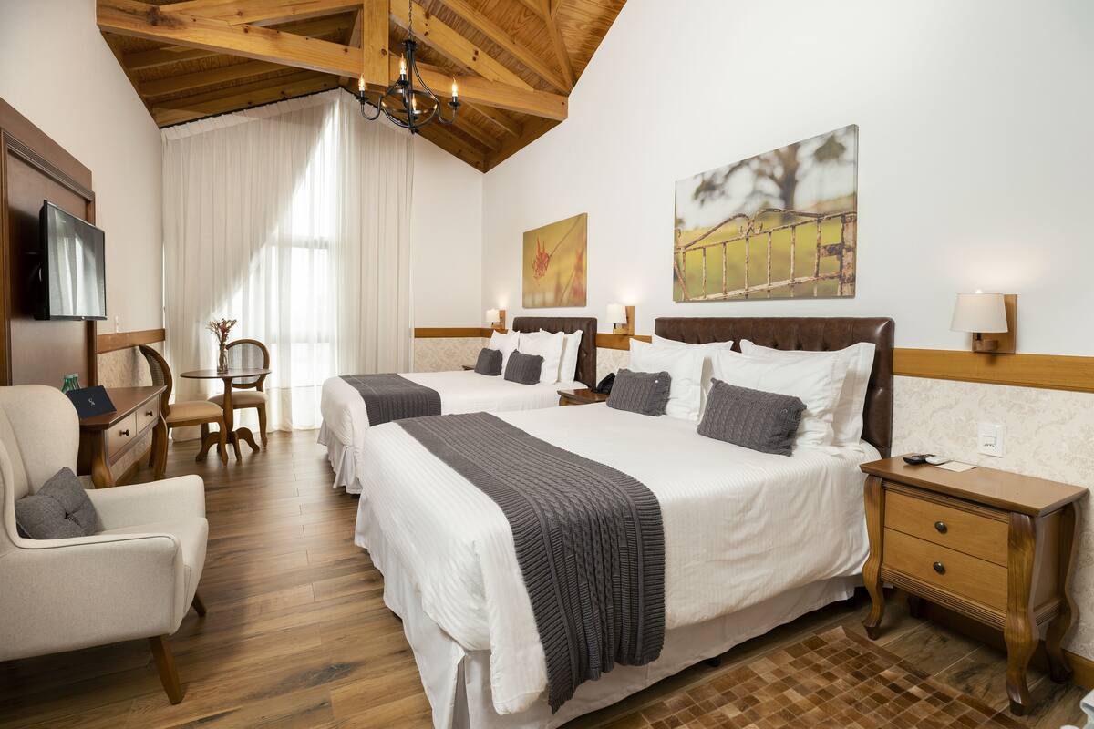 A hotel room with two beds, a desk, a chair, a TV, and artwork on the walls.