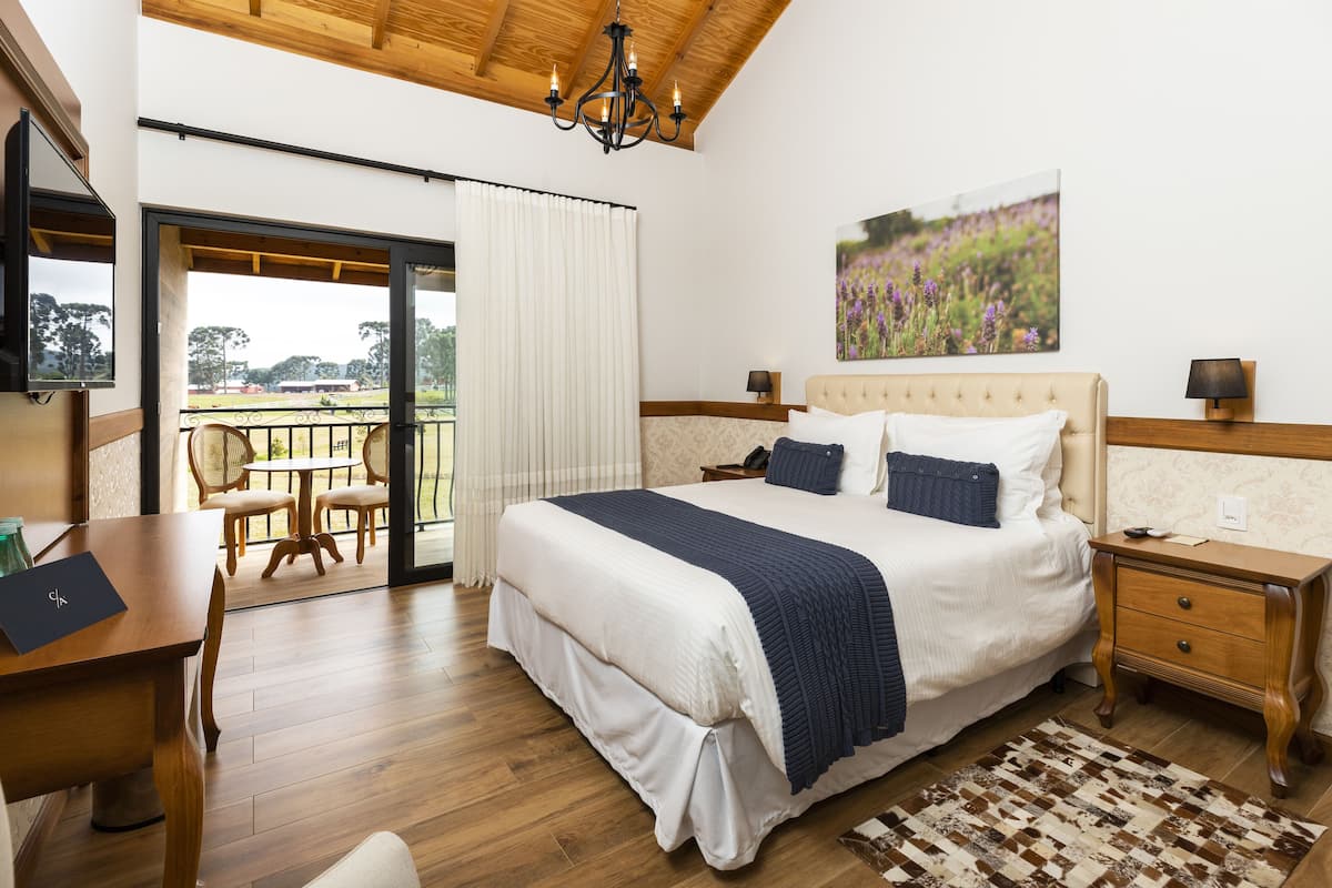 A bedroom with a large bed, a desk, and a chair, a balcony with a view, and a chandelier.