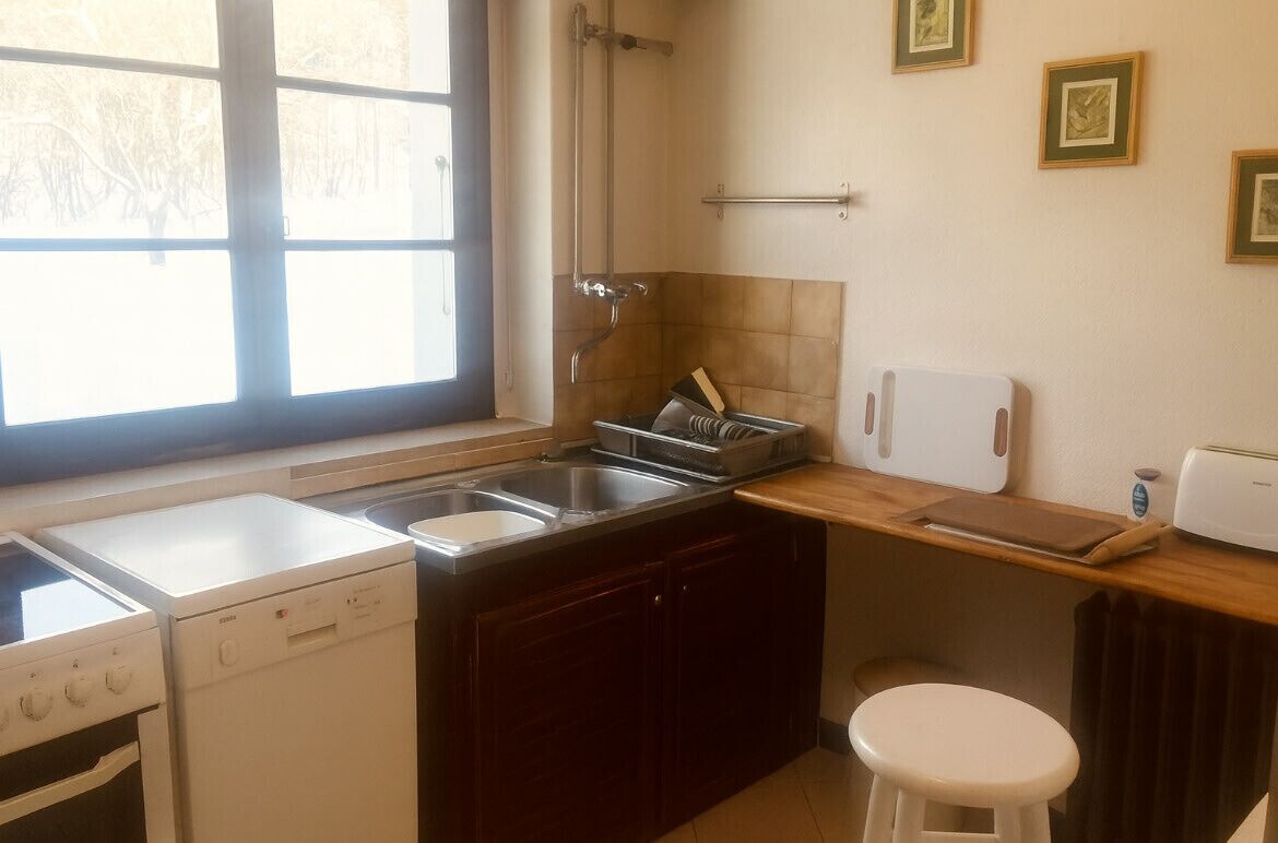 Cocina compacta con lavavajillas, estufa, pileta y un taburete pequeño.