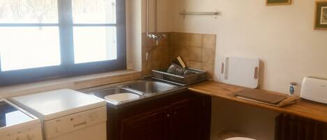 Cocina compacta con lavavajillas, estufa, pileta y un taburete pequeño.