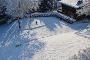 En snedækket gård med en træbænk og et hus i baggrunden.