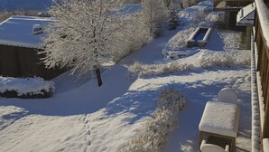 A snow-covered outdoor area with a wooden deck, a chair, and a table.