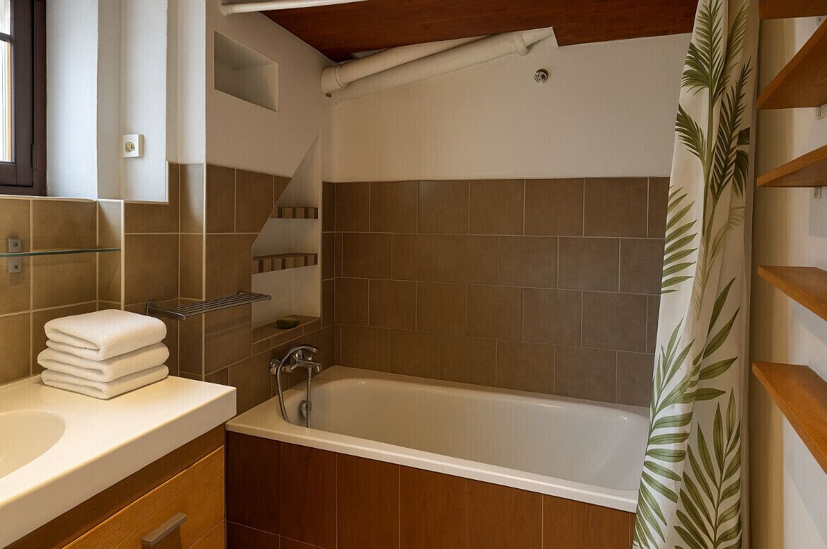 Une salle de bain avec une baignoire, une cabine de douche en verre et un meuble-lavabo en bois sur lequel sont pliés des serviettes.