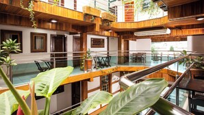 Un interior con varios niveles, paneles de madera, barandales de vidrio y plantas en macetas.