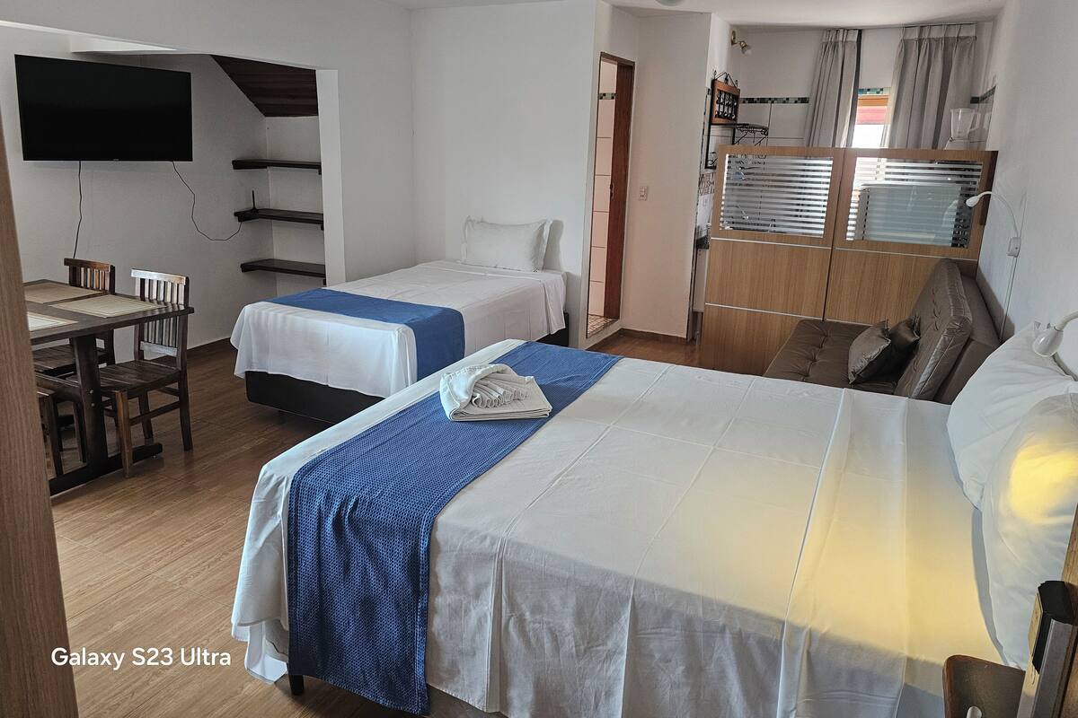 Quarto de hotel com duas camas, uma escrivaninha, uma televisão e uma kitchenette.