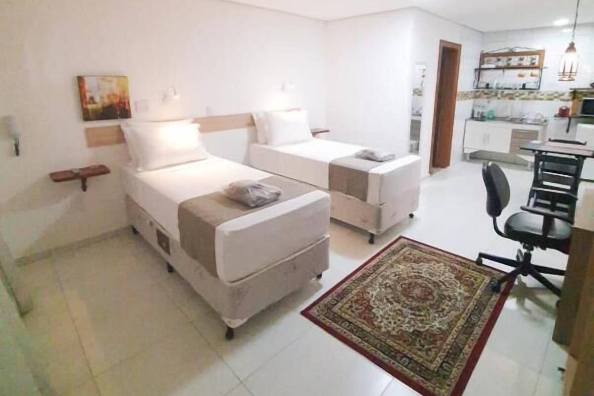 Quarto moderno com duas camas, uma pequena escrivaninha e uma kitchenette.