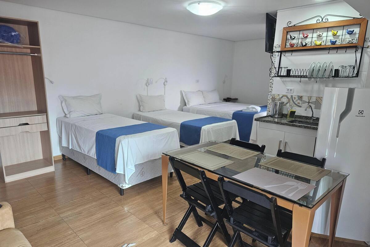 Quarto de hotel com duas camas de solteiro, uma kitchenette pequena, uma mesa de jantar e um guarda-roupa.